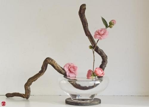 a glass bowl filled with pink flowers on top of a white table next to a branch