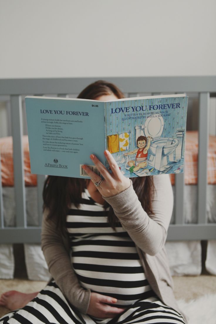 a pregnant woman sitting on the floor reading a children's book love you forever