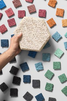 a hand holding a block of colored sand next to small blocks of black, red, and blue