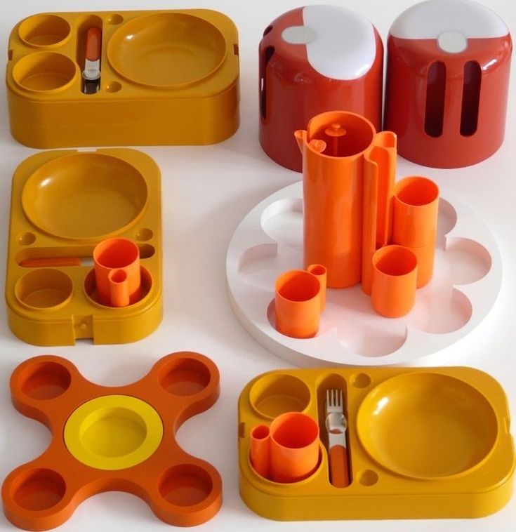 an assortment of plastic dishes and utensils on a white table top with orange cups