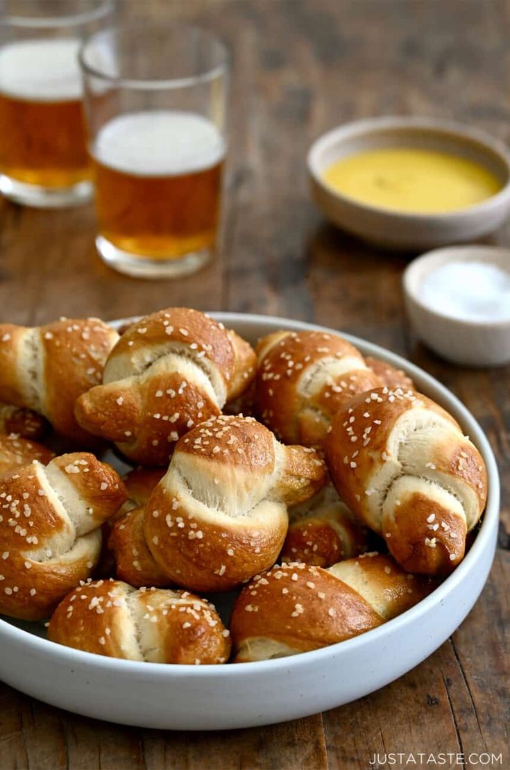 a bowl filled with pretzels sitting on top of a wooden table next to two glasses