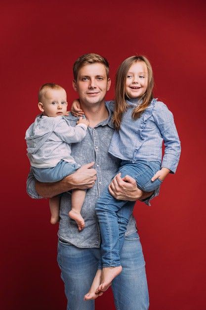 a man and woman holding a baby in front of a red background with the child on his lap