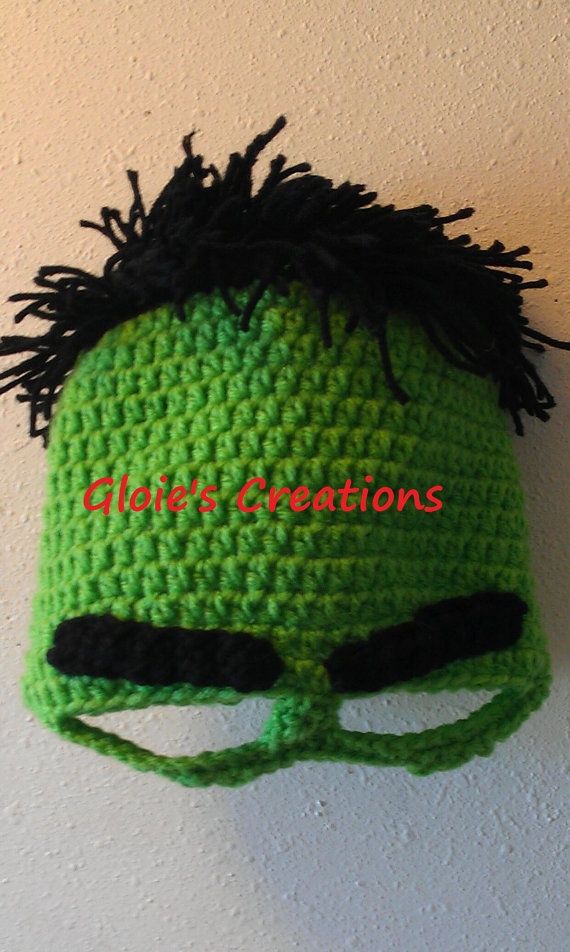 a crocheted green hat with black hair and eyes is hanging on the wall