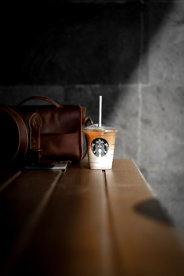 a starbucks drink sitting on top of a wooden table next to a brown leather bag