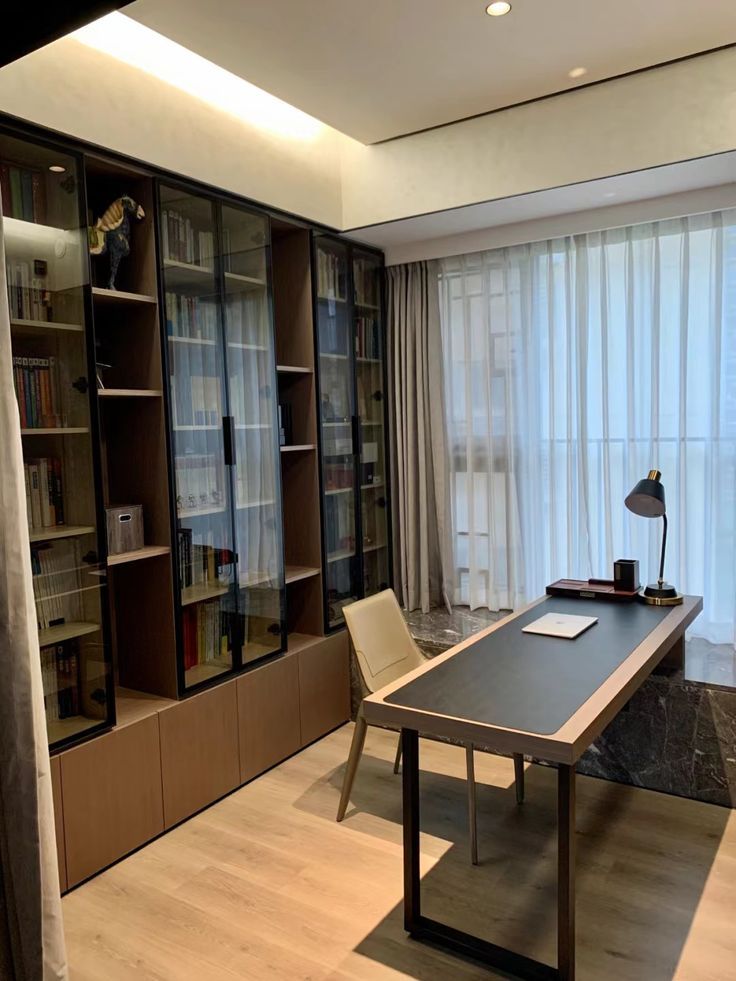 a room with a desk, bookshelf and chair in it next to a window