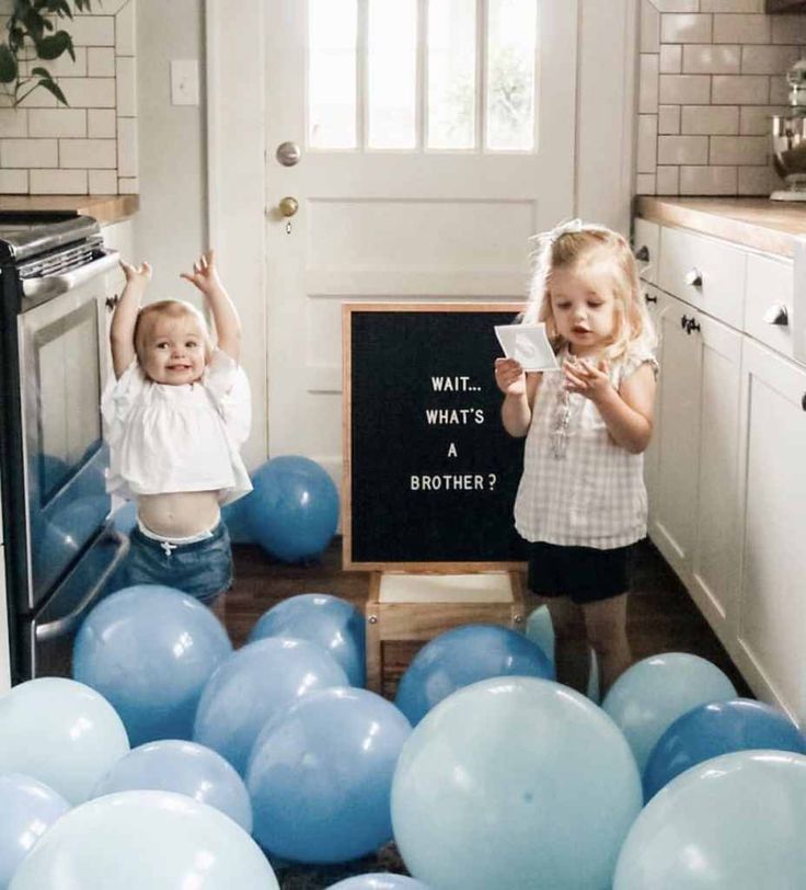 two young children standing in front of balloons and a chalkboard that says wait what's a brother?