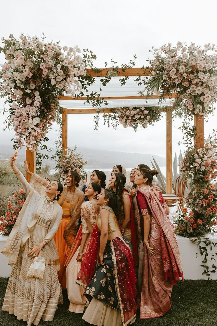 a group of women standing next to each other in front of a flower covered arch