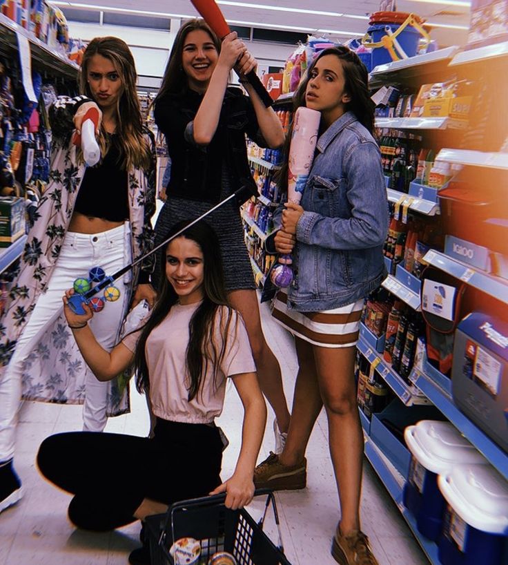 four girls are standing in a grocery store and one is holding an umbrella