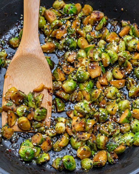 the brussel sprouts are being cooked in a skillet with a wooden spoon