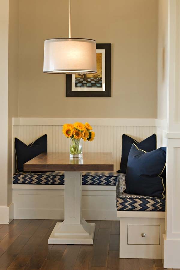 a dining room table with two blue and white pillows on the bench next to it