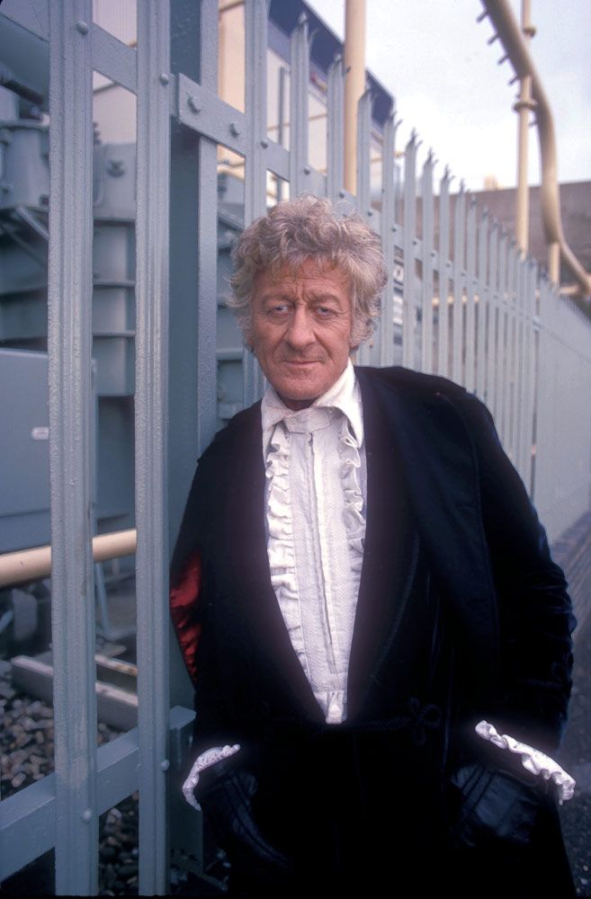 an older man in a tuxedo leaning against a metal fence with his hands on his hips