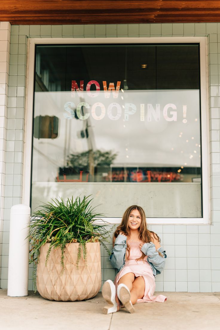 a woman sitting on the ground in front of a store window with a potted plant