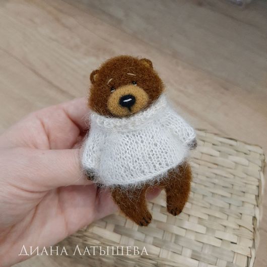 a hand holding a small stuffed bear in a sweater