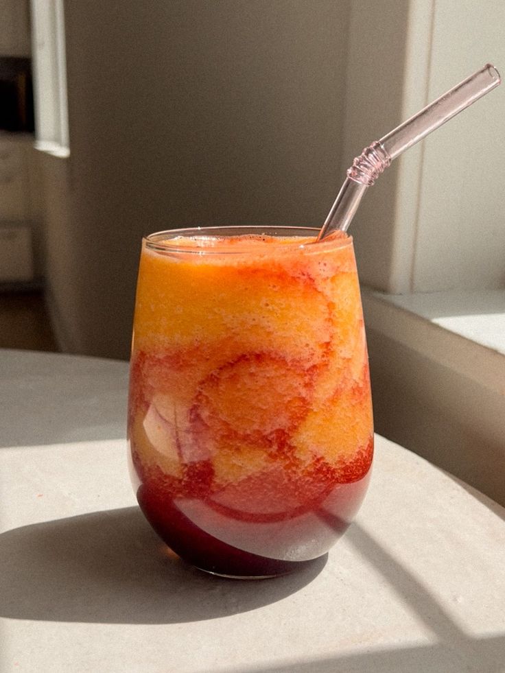 a glass filled with liquid sitting on top of a white table next to a window