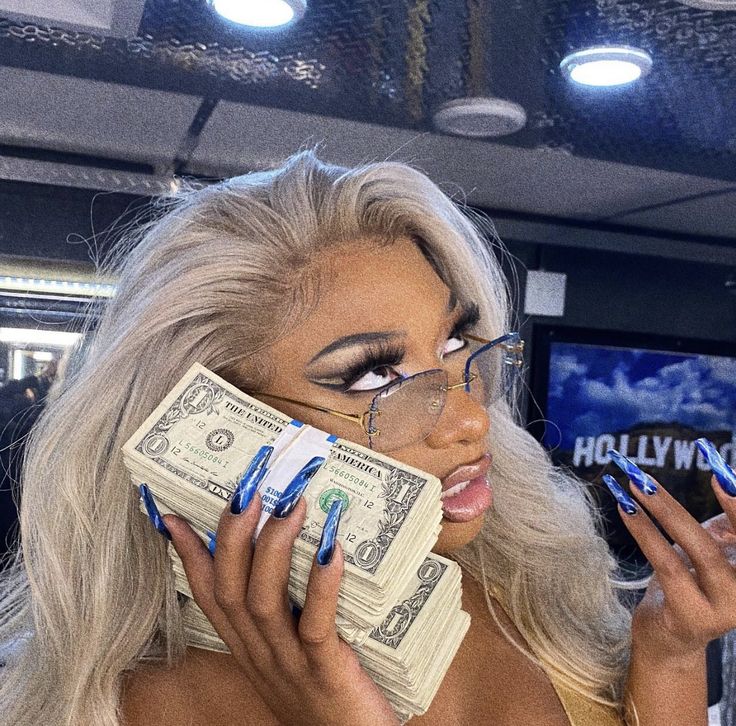 a woman with blue nails and makeup holding money in her hand while talking on the phone