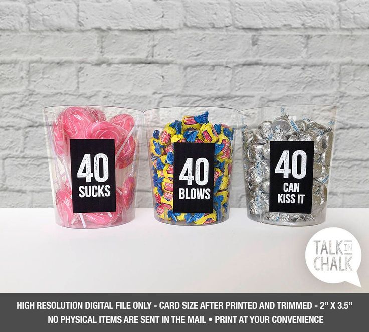 three plastic cups filled with candies on top of a white table next to a brick wall