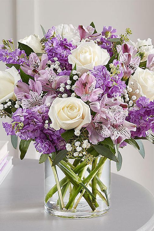 a vase filled with white and purple flowers on top of a table next to a book