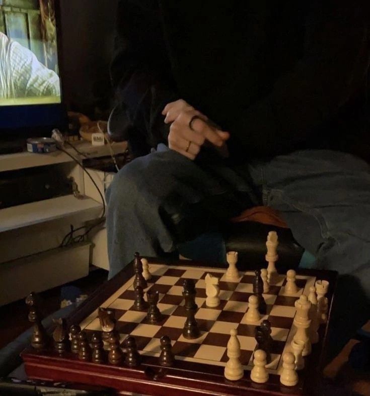 a man sitting in front of a tv playing chess with his hands on the board