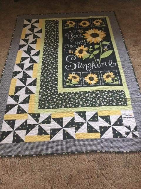 a quilt on the floor with sunflowers and words written in black, yellow and white