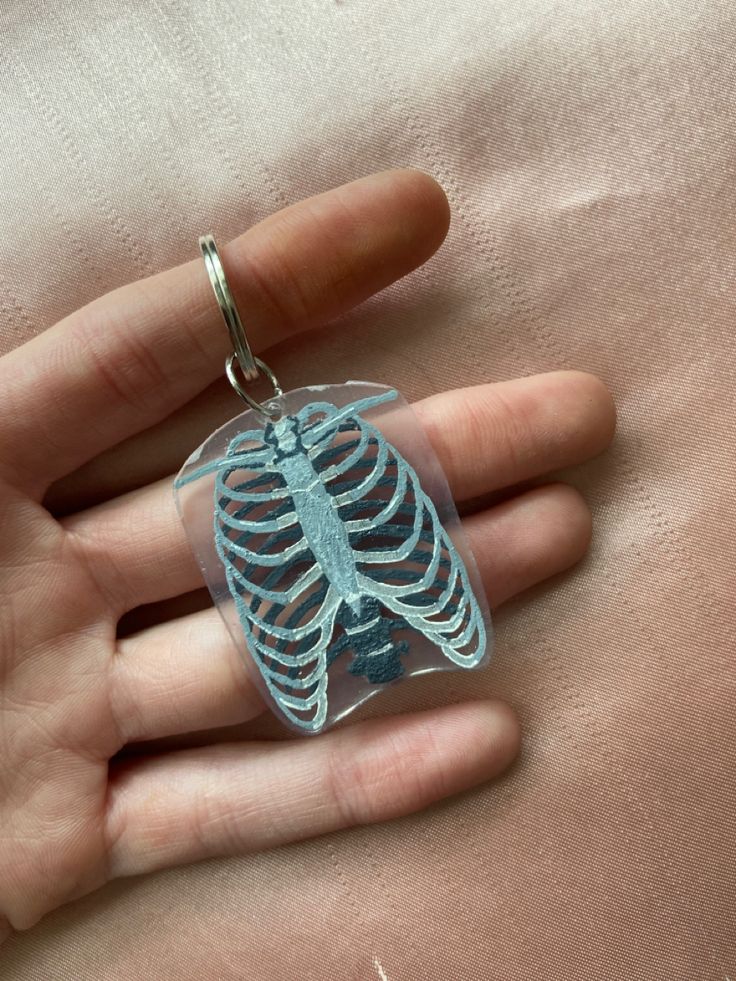 a hand holding a skeleton keychain on top of a pink sheeted surface