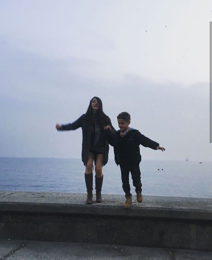 two people standing on the edge of a pier near the water with their arms outstretched