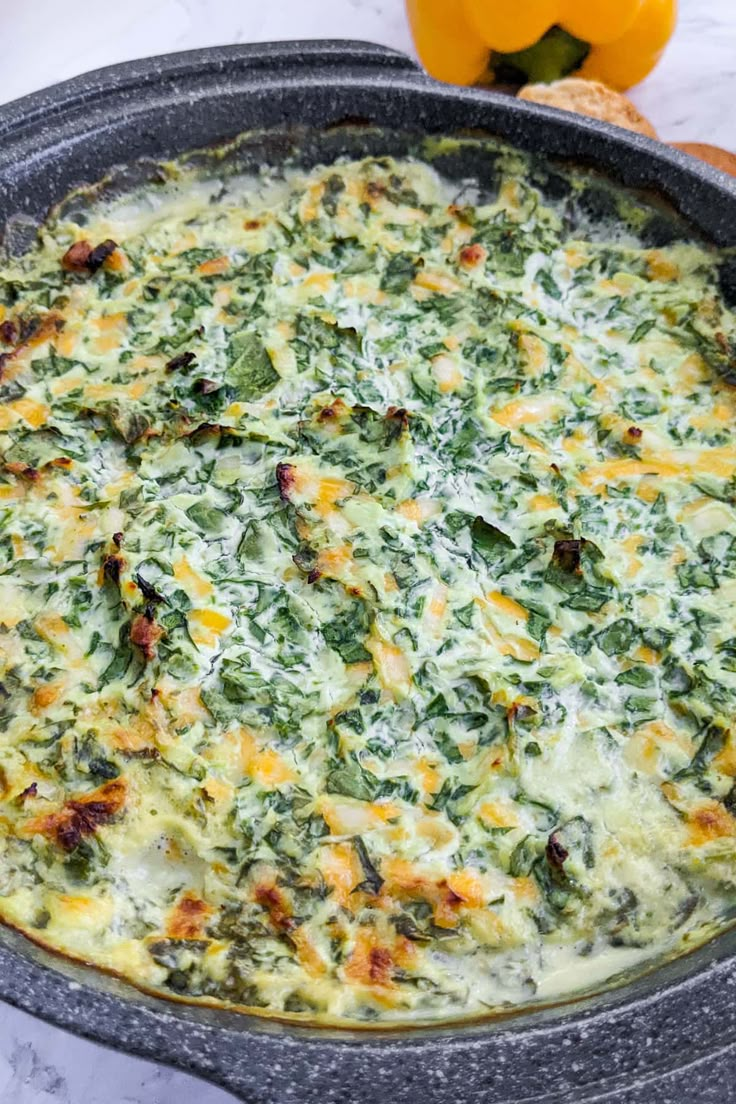 a pizza with cheese and spinach in a pan on a table next to an orange