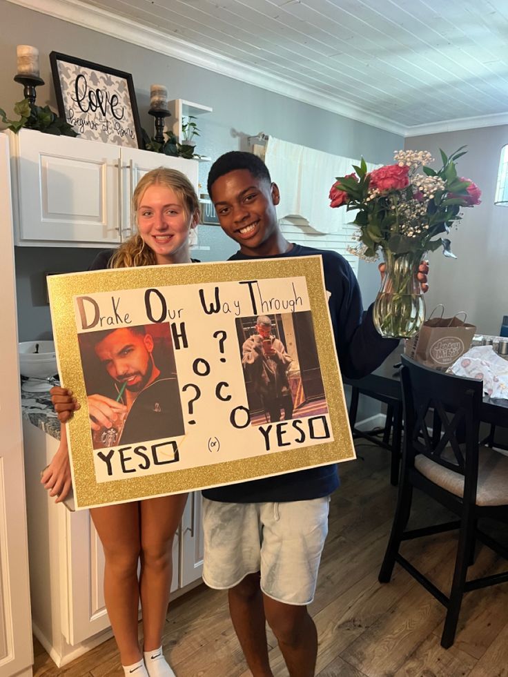 two people standing in a kitchen holding up a sign