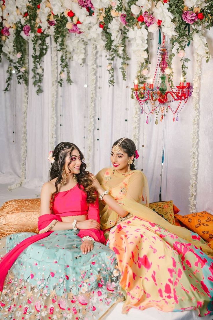 two women sitting next to each other in front of a flower covered stage with flowers hanging from the ceiling