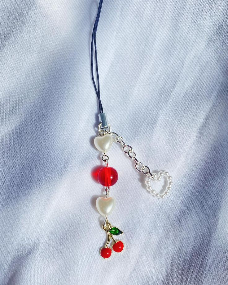 a necklace with cherries hanging from it's side on a white shirt background