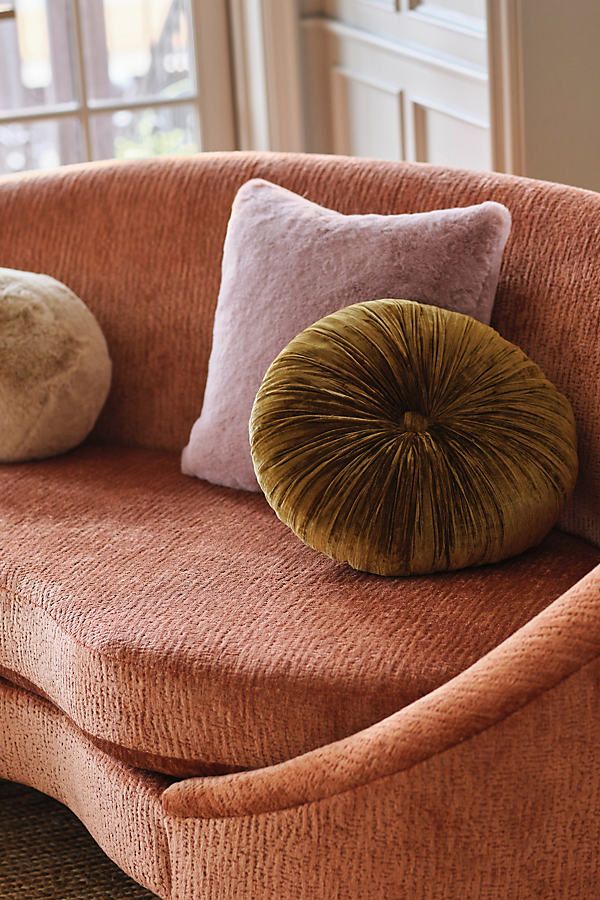 an orange couch with two pillows and a pillow on it's back in front of a window