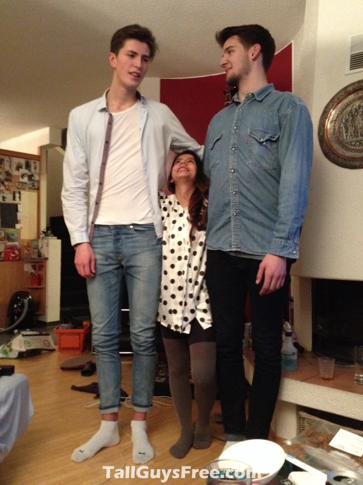 two men and a woman are standing in a living room with their feet on the floor