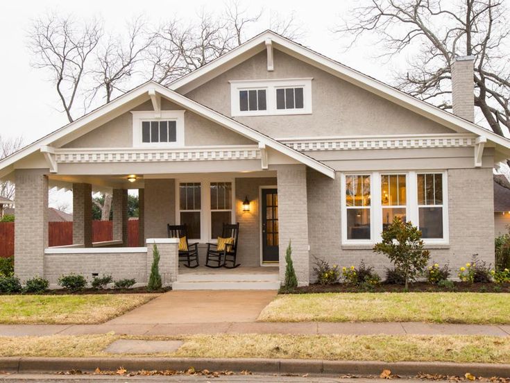 a gray house with white trim on the front door and two chairs in the front yard