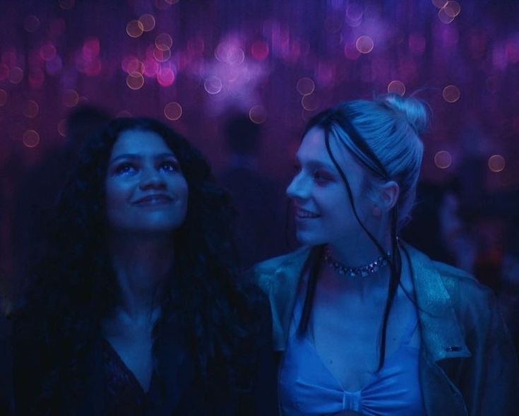 two women standing next to each other in a room with lights on the wall behind them