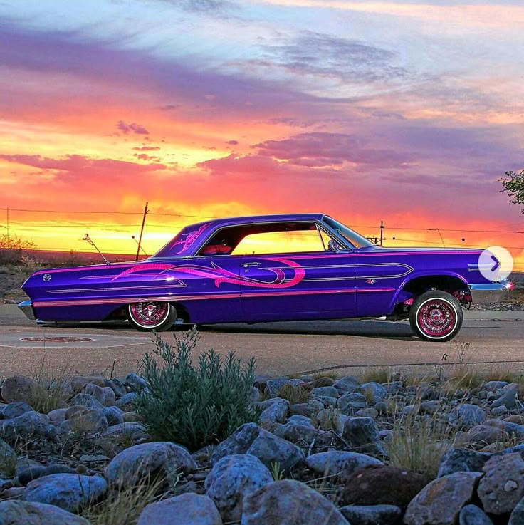 an old purple car parked in front of a sunset