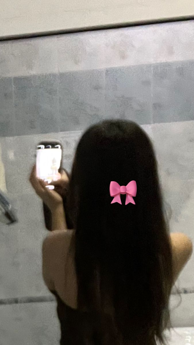 a woman taking a selfie in the bathroom with her cell phone and pink bow