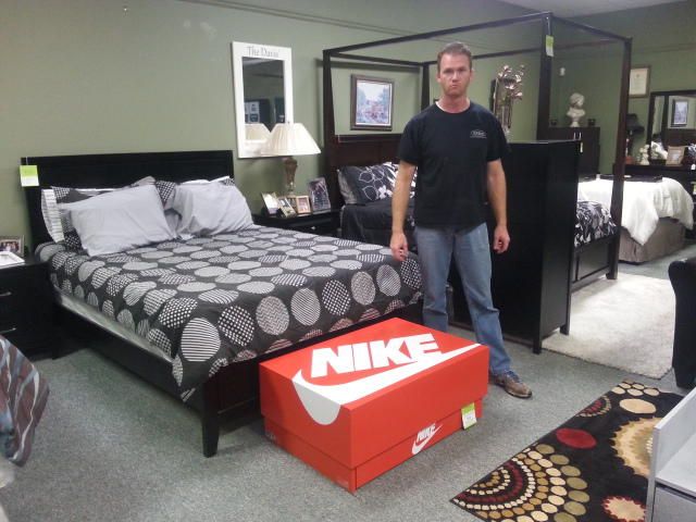 a man standing next to a bed with a nike box on the floor in front of it