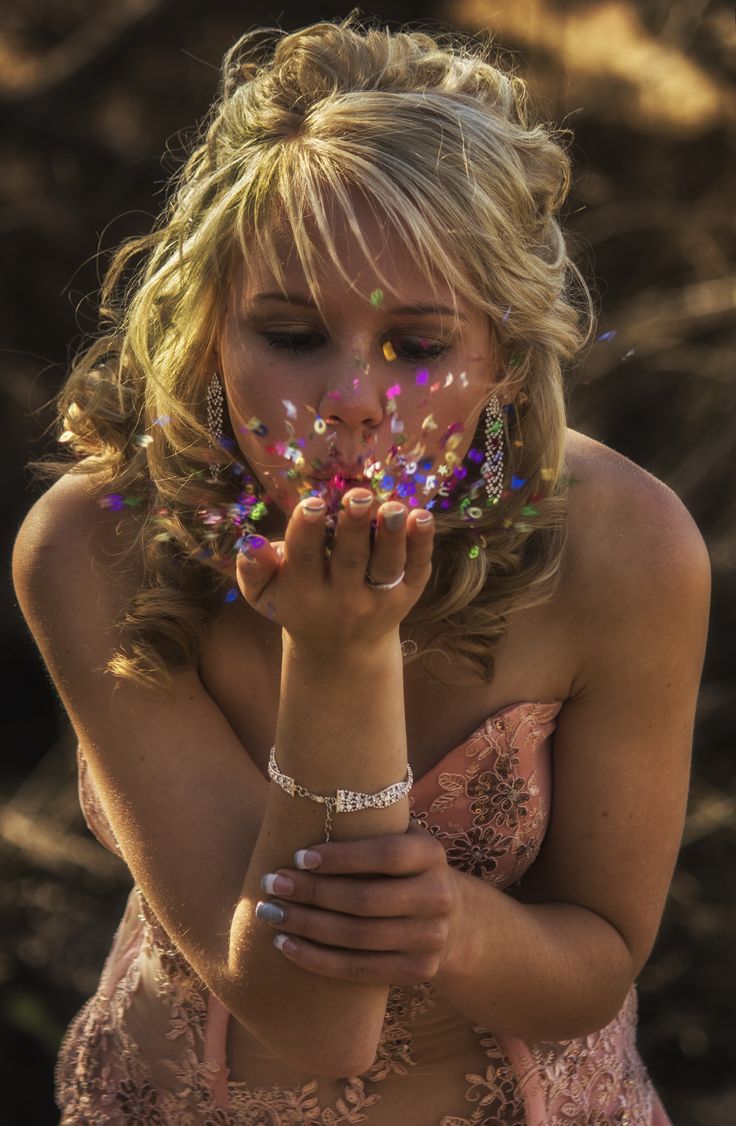 a woman in a pink dress blowing confetti on her face