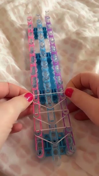 two hands are holding small plastic objects on a white sheet with pink and blue strips