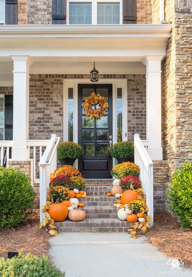 front porch decorated for fall with pumpkins and gourds on the steps leading up to the door