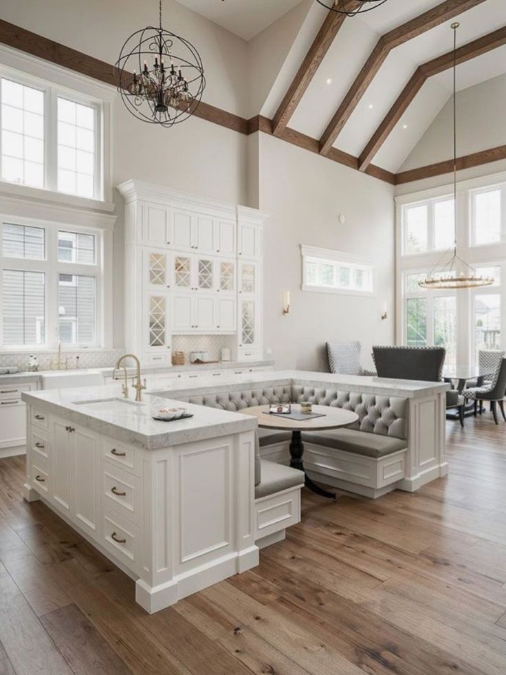 a large open kitchen with white cabinets and wood flooring, along with two chandeliers hanging from the ceiling