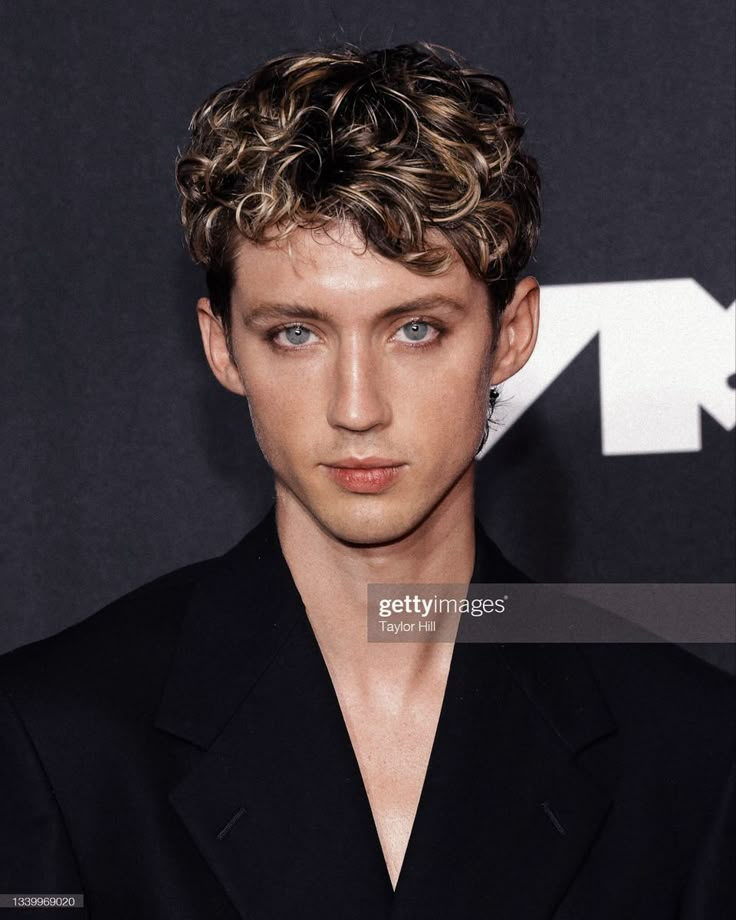 a young man with curly hair and blue eyes poses for the camera at an event