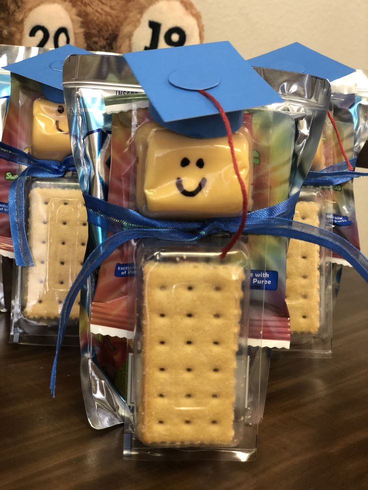 some crackers are wrapped in plastic and have graduation hats on them, with a teddy bear wearing a blue cap