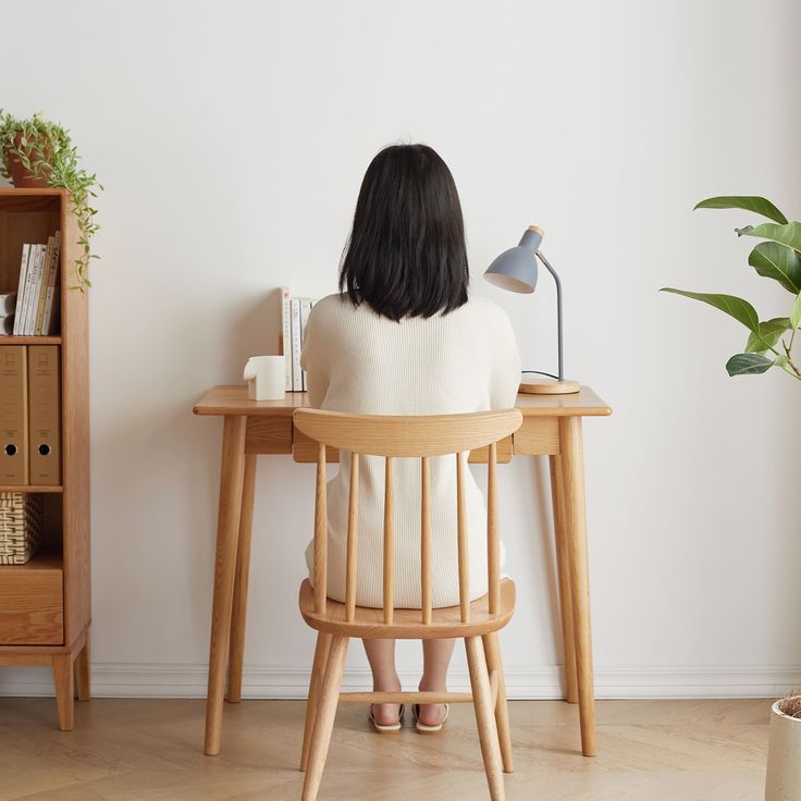 a woman sitting at a desk with a lamp on it's side and her back turned to the camera