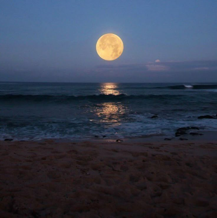 the full moon is setting over the ocean