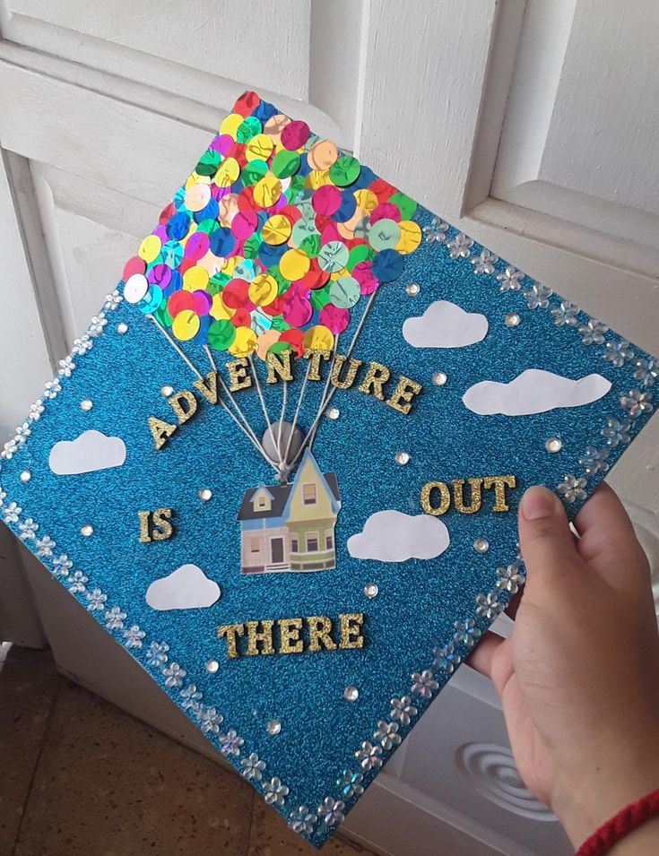 someone is holding up a blue graduation cap that says adventure is out there with balloons on it