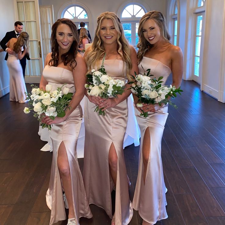 three beautiful women standing next to each other wearing dresses with slits on the sides