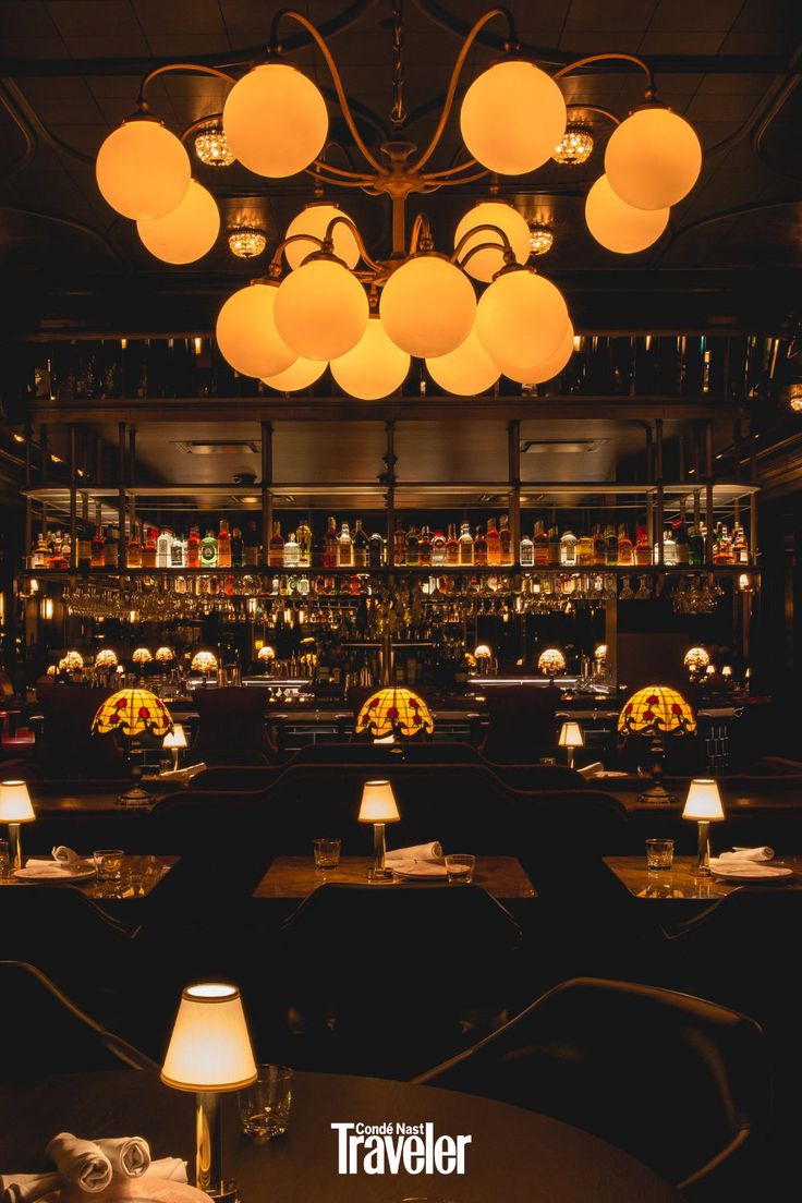 a dimly lit restaurant with many tables and lamps hanging from the ceiling over them,