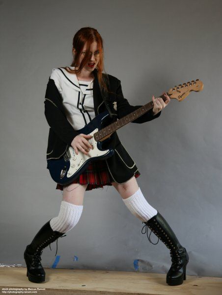 a woman with red hair and black boots playing an electric guitar while wearing a kilt