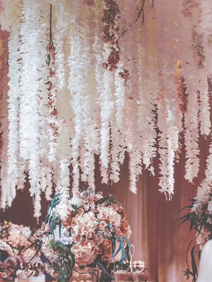 an arrangement of flowers hanging from the ceiling in a room with pink walls and curtains