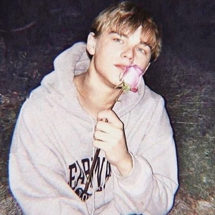 a young man sitting on the ground with a flower in his mouth